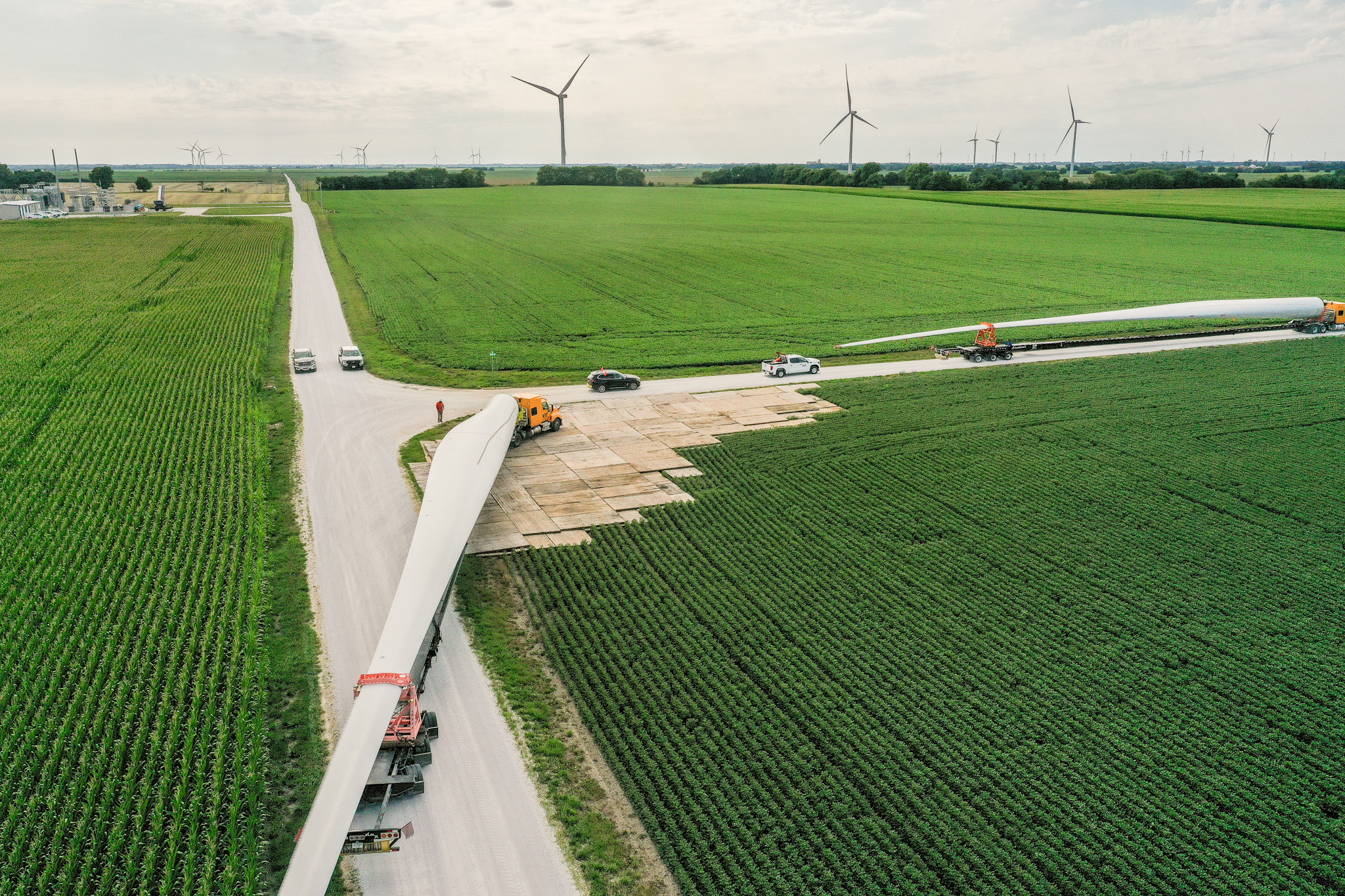 Wind turbine blade delivery across a stabilized access road constructed with matting solutions, enabling safe transport through agricultural terrain for renewable energy infrastructure projects.